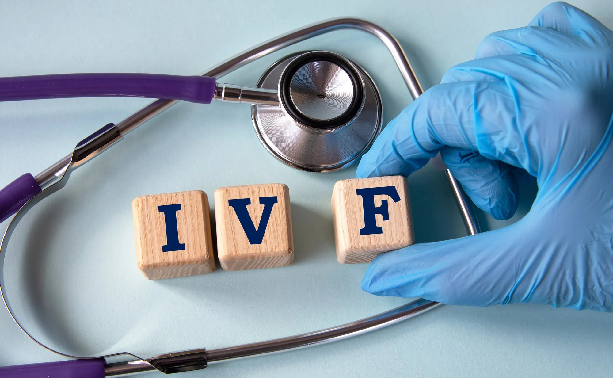 Gloved hand placing wooden blocks spelling IVF beside a stethoscope